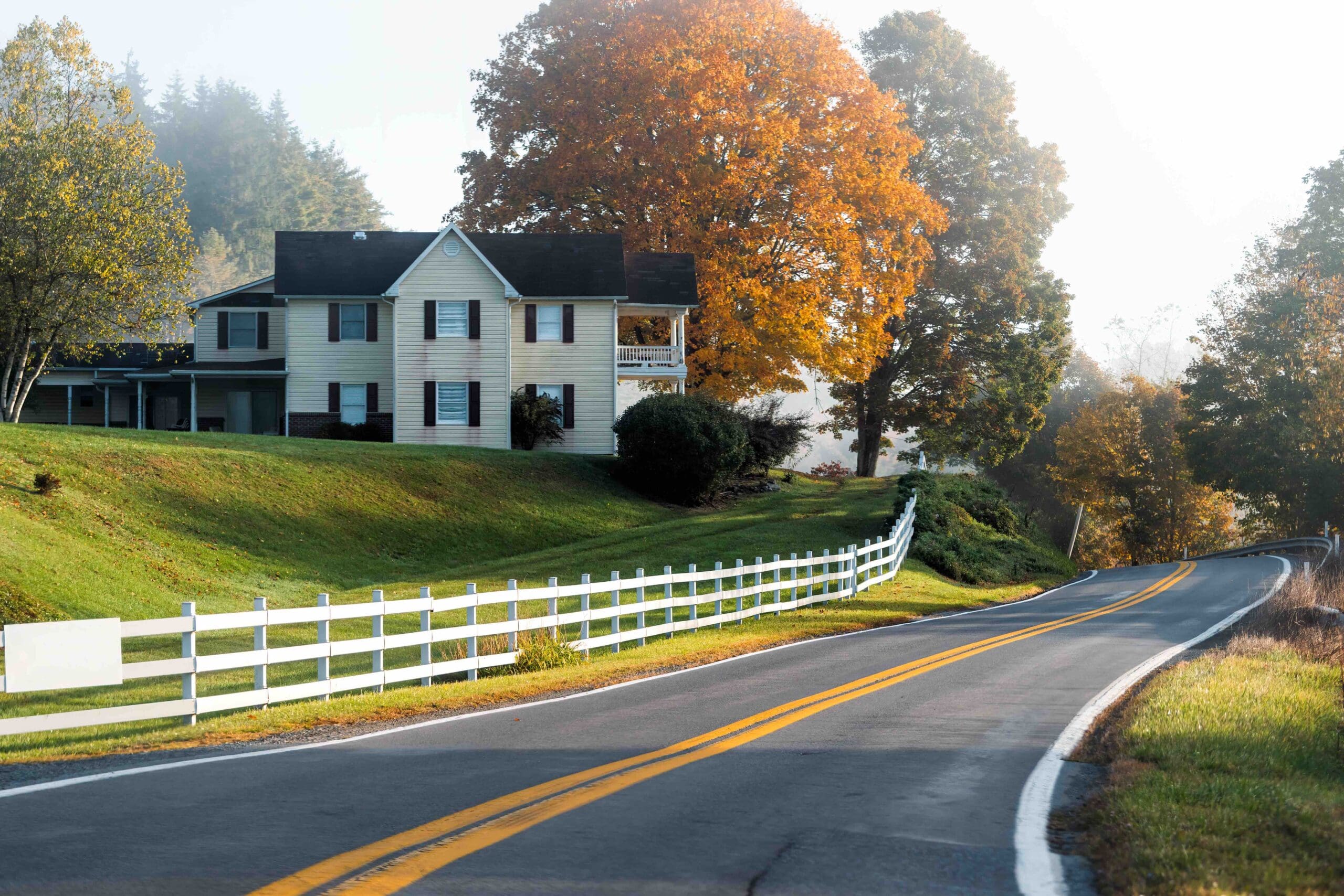 Roadside farmhouse house in countryside rural road highway in West Virginia, USA by mountain forest with colorful autumn fall trees foliage at sunrise morning