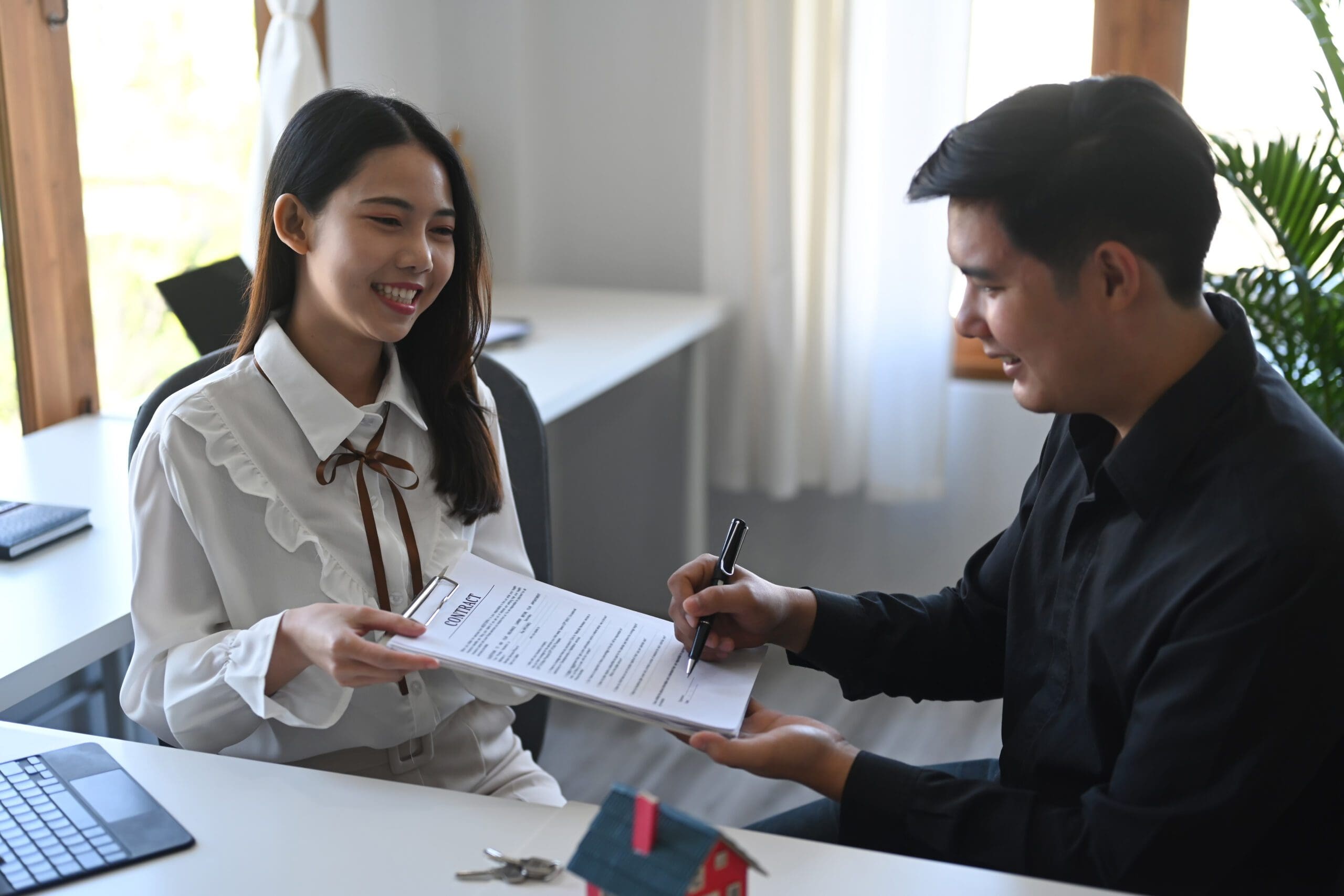 Happy young asian man signing rental contract with real estate b