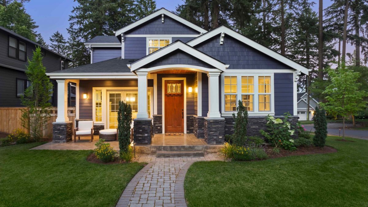 Luxury Home Exterior at Night: Beautiful New House with Green Grass and Landscaping at Twilight.Has Covered Porch and Glowing Interior Lights.