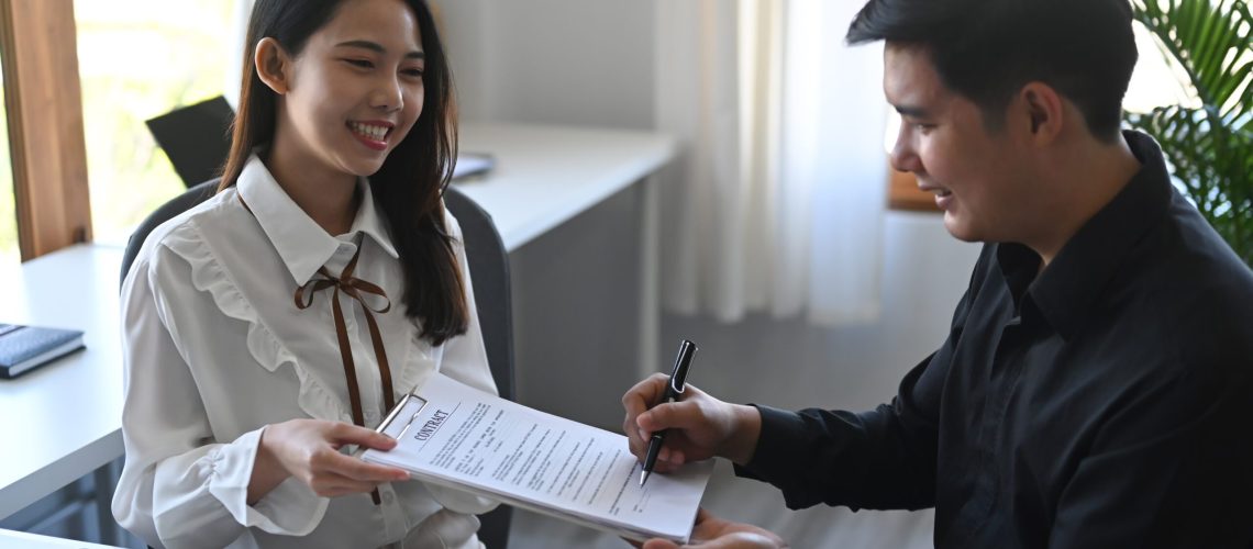 Happy young asian man signing rental contract with real estate b